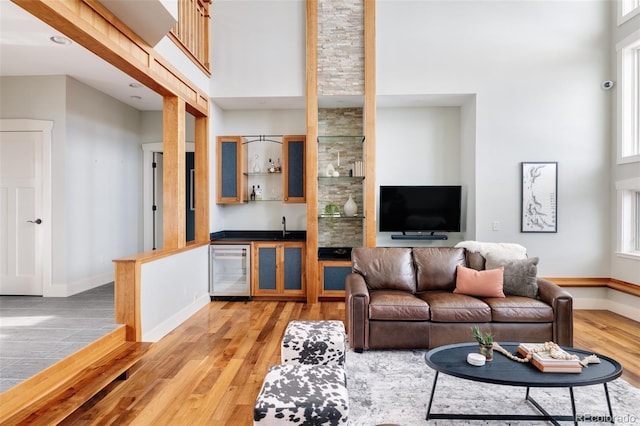 living room with indoor wet bar, a towering ceiling, wine cooler, a wealth of natural light, and light hardwood / wood-style floors