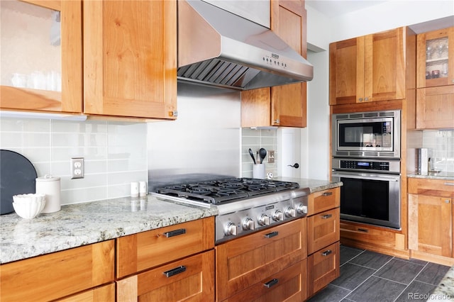 kitchen featuring range hood, light stone countertops, decorative backsplash, and stainless steel appliances