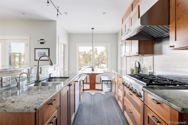 kitchen with hanging light fixtures, sink, a kitchen island with sink, and light stone counters