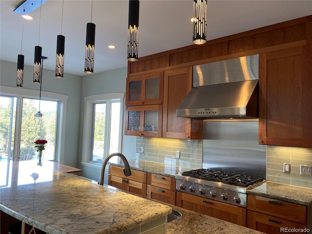 kitchen with light stone counters, decorative light fixtures, stainless steel gas cooktop, and wall chimney range hood