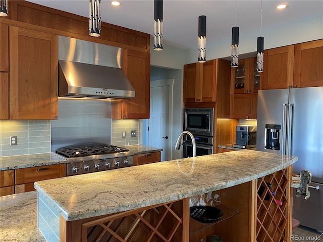 kitchen with pendant lighting, backsplash, stainless steel appliances, a center island with sink, and wall chimney exhaust hood