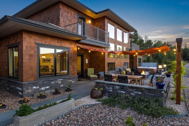 back house at dusk with a balcony, a hot tub, and a patio area