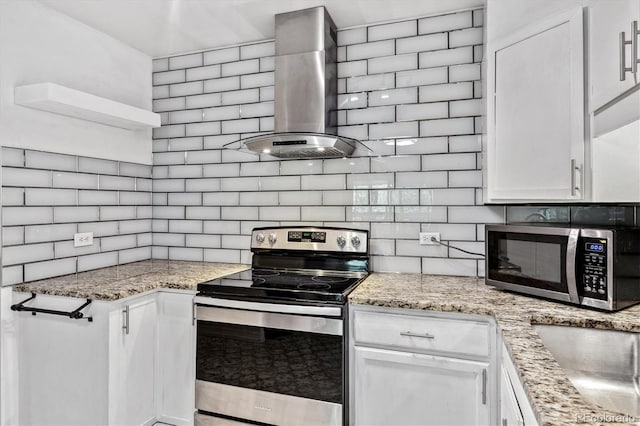 kitchen with appliances with stainless steel finishes, light stone counters, wall chimney exhaust hood, and white cabinetry