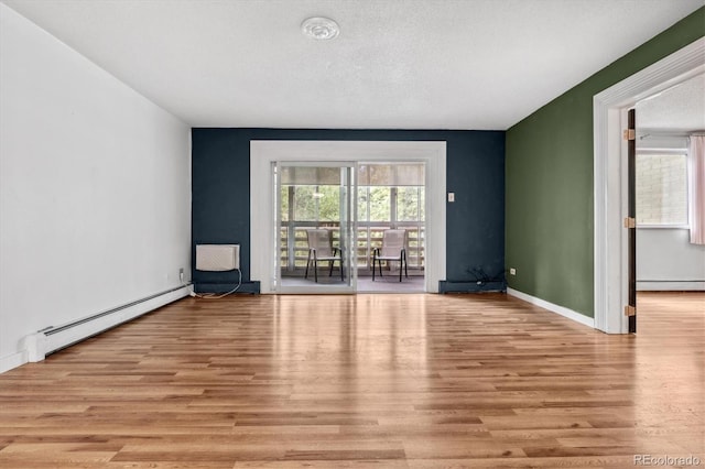 spare room featuring a baseboard heating unit, light wood-type flooring, and a textured ceiling