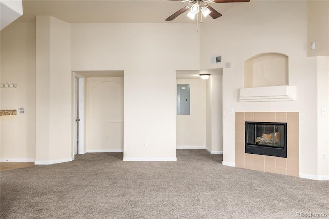 unfurnished living room featuring a tile fireplace, electric panel, carpet flooring, ceiling fan, and a towering ceiling