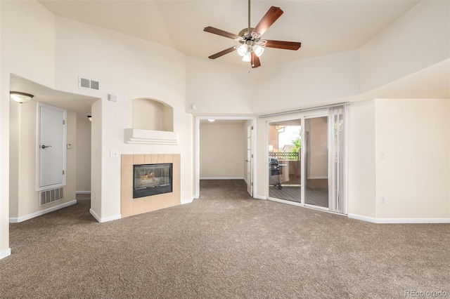 unfurnished living room featuring carpet flooring, ceiling fan, a towering ceiling, and a tile fireplace