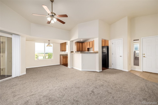 unfurnished living room with light carpet, ceiling fan with notable chandelier, and a high ceiling