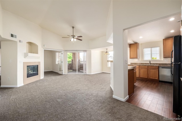 unfurnished living room with ceiling fan, sink, dark colored carpet, high vaulted ceiling, and a fireplace