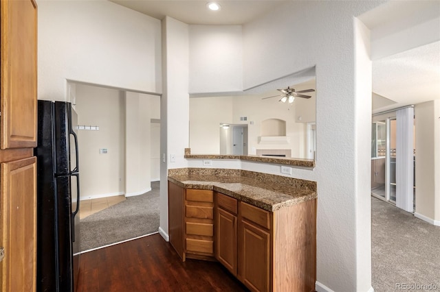 kitchen featuring black fridge, ceiling fan, dark stone counters, and dark carpet