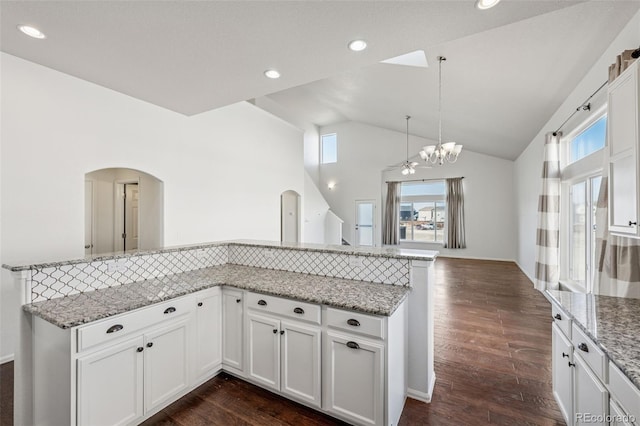 13135 Devils Thumb Pl, Peyton, CO 80831 - kitchen with arched walkways, lofted ceiling, white cabinets, dark wood-style floors, and light stone counters