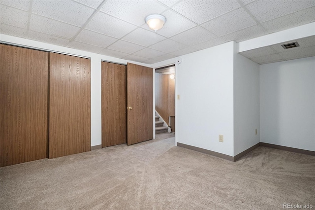 unfurnished bedroom with multiple closets, a paneled ceiling, and light colored carpet