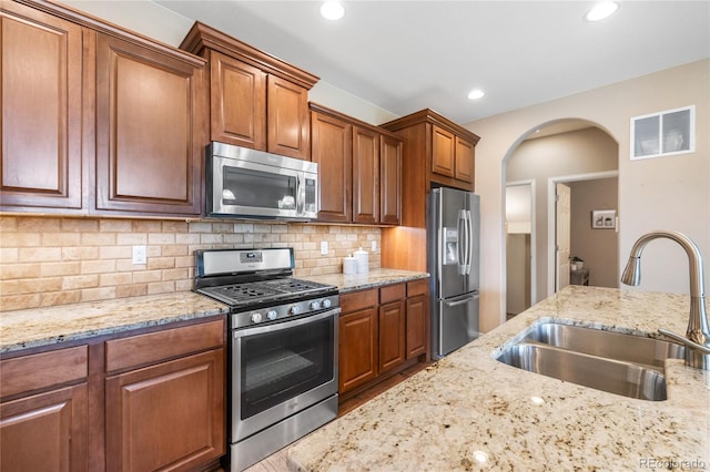 9530 Gray St, Westminster, CO 80031 - kitchen featuring stainless steel appliances, arched walkways, light stone counters, decorative backsplash, and brown cabinetry