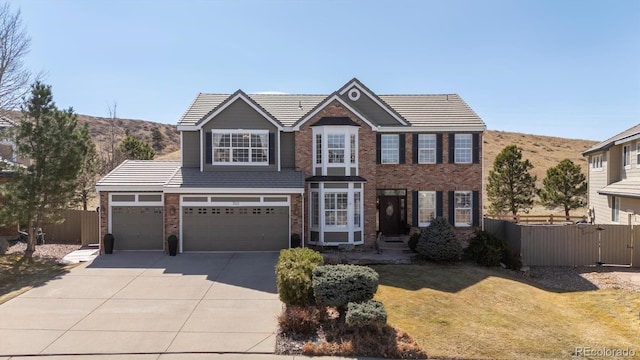 view of front of house featuring a tiled roof, brick siding, concrete driveway, and fence