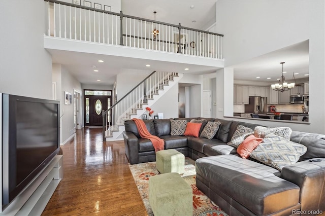 living area featuring stairway, wood finished floors, a towering ceiling, and a chandelier