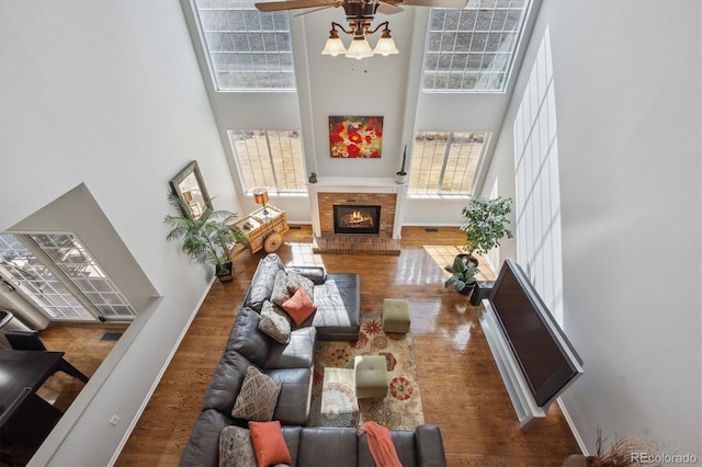 living room with baseboards, wood finished floors, a towering ceiling, and a fireplace