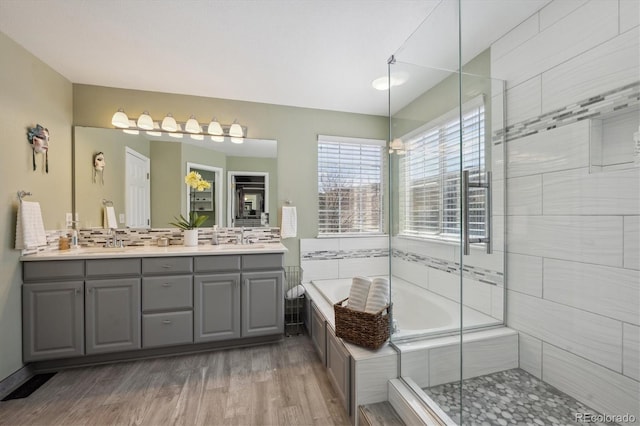 full bathroom with a shower stall, a bath, wood finished floors, and a sink