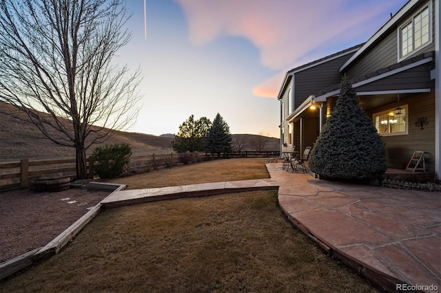 yard at dusk featuring a mountain view, a patio, and fence