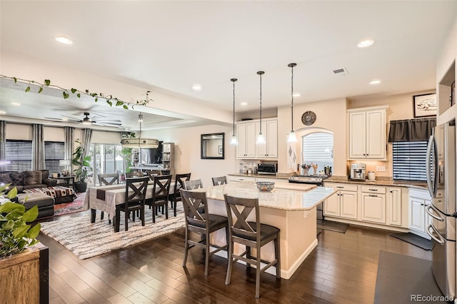 kitchen with pendant lighting, ceiling fan, light stone countertops, a breakfast bar, and a kitchen island