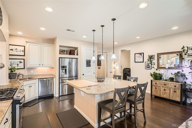 kitchen with a breakfast bar area, light stone counters, a center island, hanging light fixtures, and stainless steel appliances