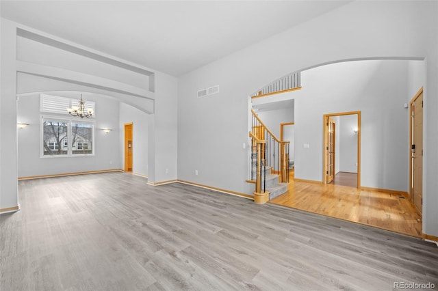 unfurnished living room with an inviting chandelier, a towering ceiling, and light hardwood / wood-style floors