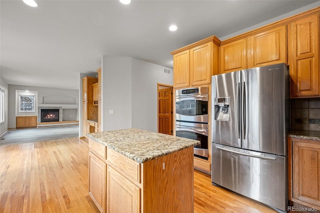 kitchen featuring light stone countertops, light hardwood / wood-style flooring, stainless steel appliances, and a center island