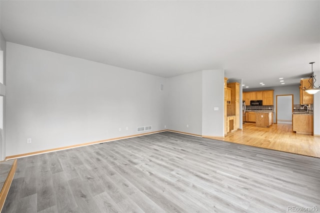 unfurnished living room featuring sink and light hardwood / wood-style flooring