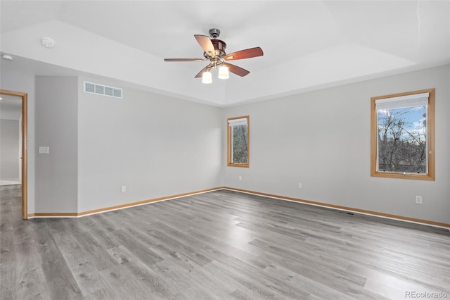 spare room featuring a raised ceiling, ceiling fan, and light wood-type flooring