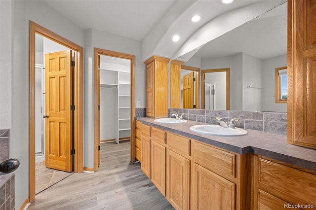 bathroom featuring vanity, a shower with shower door, hardwood / wood-style floors, and decorative backsplash