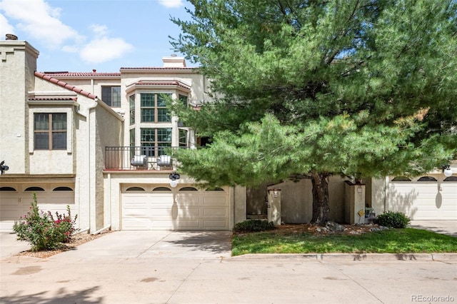 1530 S Quebec Way Unit 24, Denver, CO 80231 - view of front of house with a chimney, concrete driveway, stucco siding, a balcony, and an attached garage