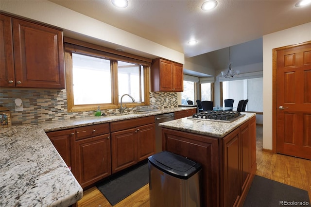 kitchen featuring sink, light hardwood / wood-style flooring, appliances with stainless steel finishes, hanging light fixtures, and light stone countertops