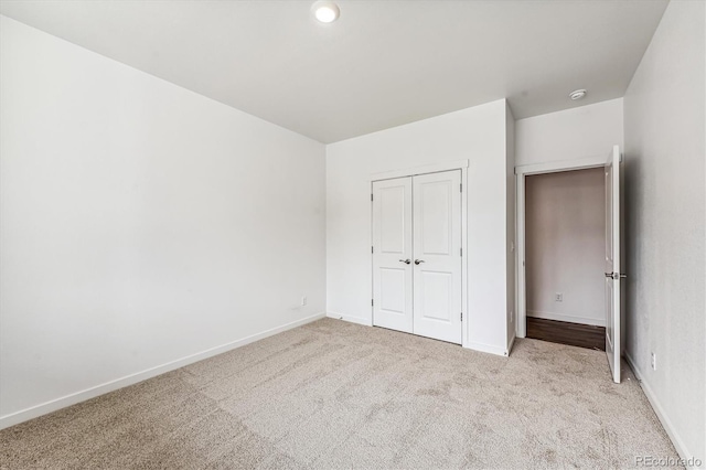 unfurnished bedroom with a closet, light colored carpet, and baseboards