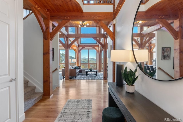 hallway featuring an inviting chandelier, light hardwood / wood-style flooring, a mountain view, a towering ceiling, and beam ceiling