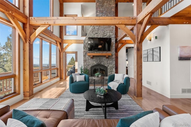 living room with plenty of natural light, a stone fireplace, light hardwood / wood-style flooring, and a high ceiling