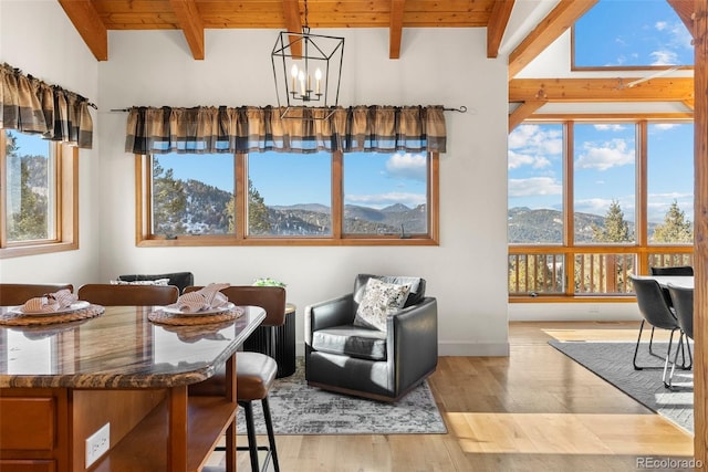 dining area with a notable chandelier, light hardwood / wood-style flooring, a mountain view, a wealth of natural light, and beam ceiling