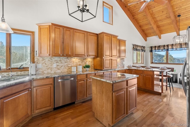 kitchen featuring sink, dishwasher, hanging light fixtures, a center island, and light stone counters