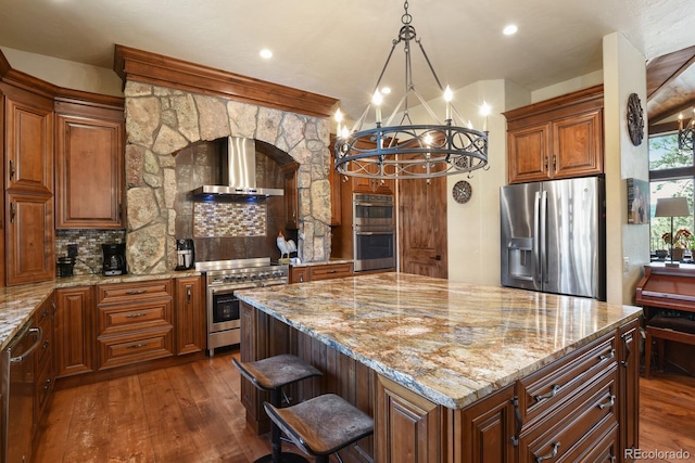 kitchen with tasteful backsplash, a kitchen island, appliances with stainless steel finishes, wall chimney range hood, and an inviting chandelier