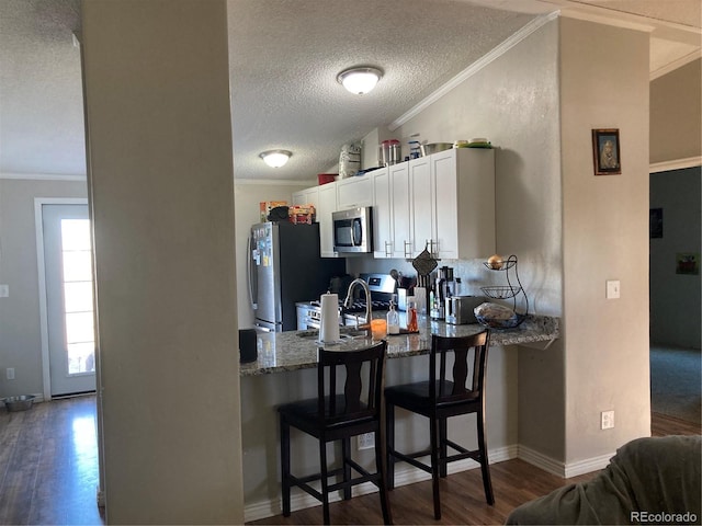 1103 Stage Dr, Fort Lupton, CO 80621 - kitchen featuring appliances with stainless steel finishes, a peninsula, a textured ceiling, crown molding, and dark wood-type flooring