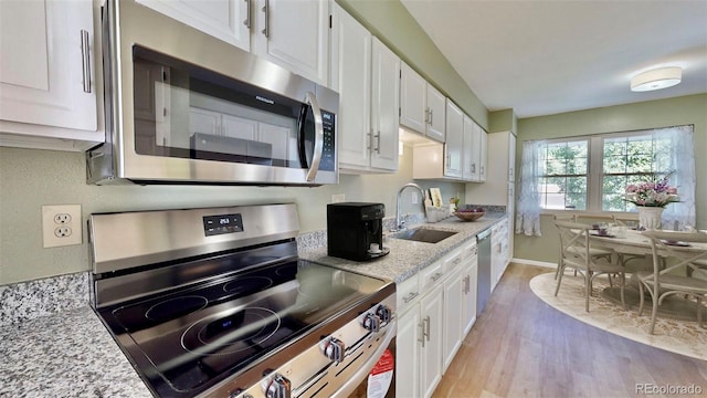 kitchen with sink, white cabinetry, stainless steel appliances, light stone countertops, and light hardwood / wood-style floors