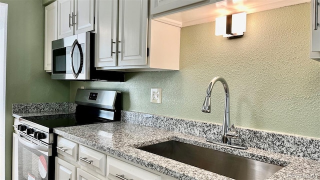 kitchen with light stone counters, stainless steel appliances, sink, and white cabinetry