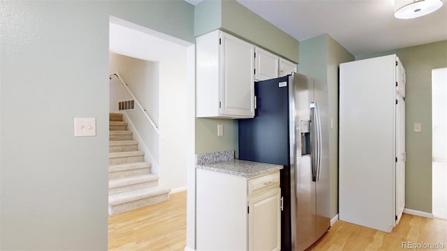 kitchen with stainless steel refrigerator with ice dispenser, light hardwood / wood-style floors, and white cabinetry