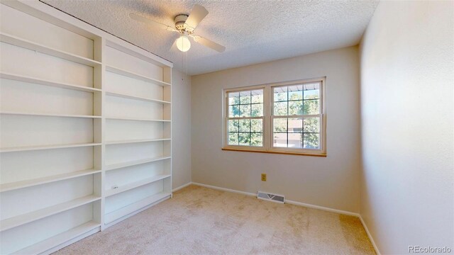 empty room featuring ceiling fan, light colored carpet, a textured ceiling, and built in features