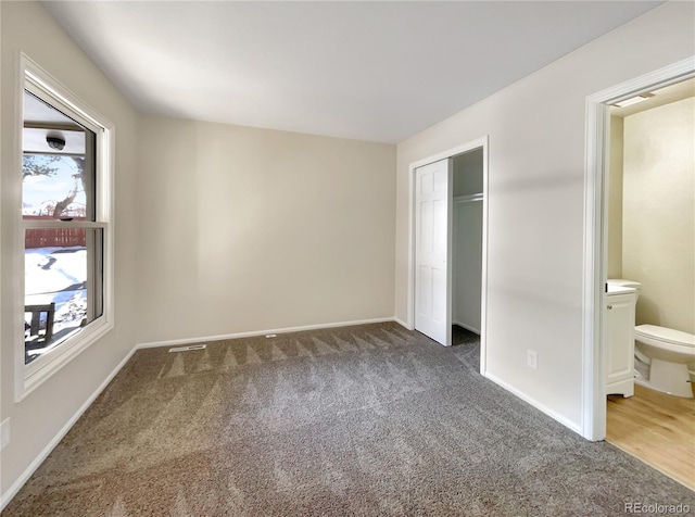 unfurnished bedroom with ensuite bath, a closet, and dark colored carpet