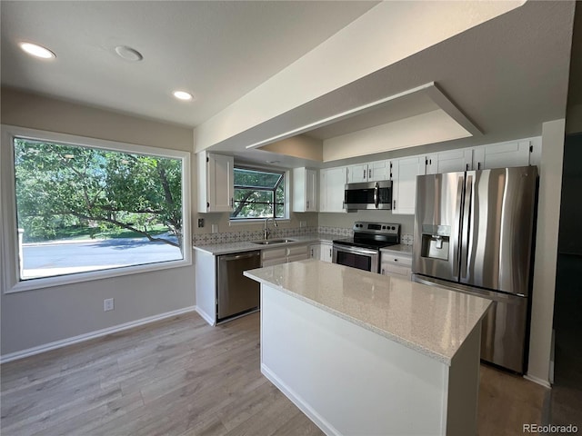 kitchen with light stone countertops, stainless steel appliances, sink, white cabinets, and a center island