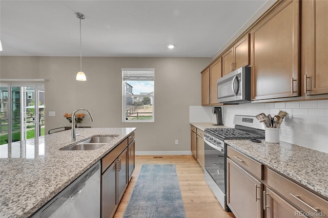 7465 E 157th Pl, Thornton, CO 80602 - kitchen with appliances with stainless steel finishes, a sink, light wood finished floors, tasteful backsplash, and pendant lighting