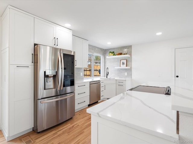 kitchen with open shelves, stainless steel appliances, backsplash, light wood-style flooring, and light stone countertops