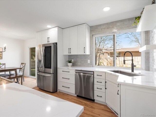 kitchen featuring light wood-style floors, a sink, stainless steel appliances, and backsplash