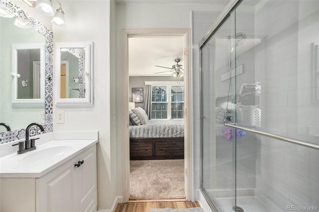 ensuite bathroom featuring ceiling fan, wood finished floors, vanity, a shower stall, and ensuite bath