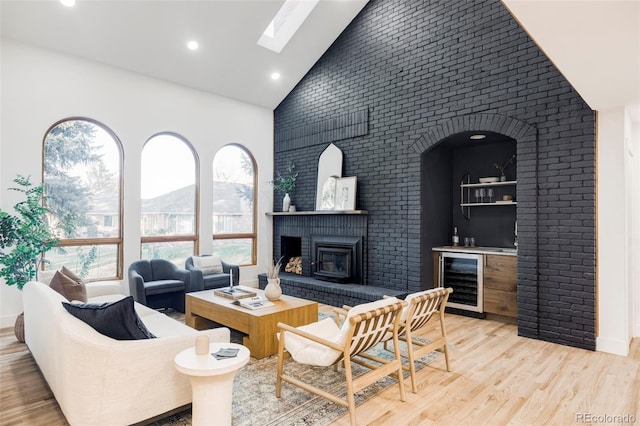 living room featuring high vaulted ceiling, wine cooler, a skylight, indoor bar, and light wood-type flooring