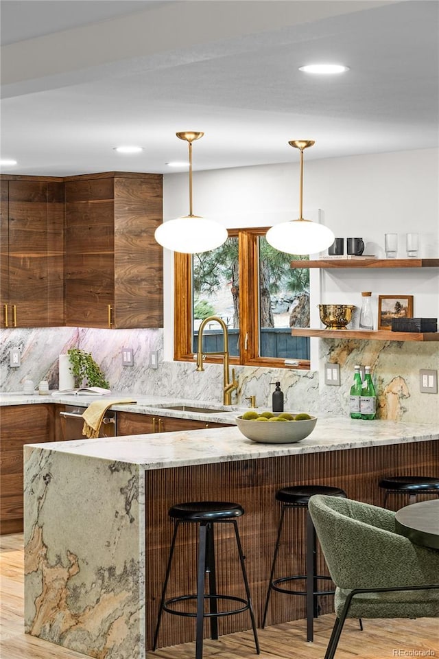 kitchen with decorative backsplash, sink, decorative light fixtures, and light hardwood / wood-style flooring