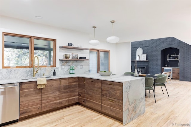 kitchen featuring light stone counters, stainless steel dishwasher, sink, a fireplace, and light hardwood / wood-style floors